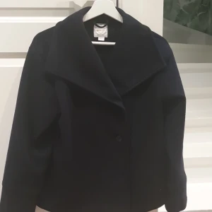 Svart kappa från Gina Tricot - Säljer en mörkblå  kappa från Gina Tricot med bred krage och knäppning framtill. Jackan har lång ärm och en stilren, enkel design som passar perfekt till många olika outfits.