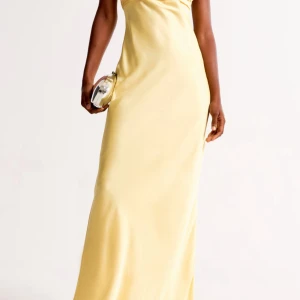 Ljusgul axelbandslös långklänning - Säljer en elegant ljusgul långklänning med axelbandslös design och draperad överdel. Klänningen har en smickrande, figurnära passform och är perfekt för speciella tillfällen. Materialet har en lätt glansig yta som ger en lyxig känsla. Klänningen är från Abercrombie & Fitch i storlek M - Tall vilket är den längre modellen. Använd 1 gång 