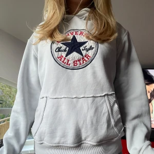 Vit hoodie från Converse - Säljer en vit hoodie från Converse med stor broderad logga på bröstet i svart och rött. Tröjan har huva, magficka och ribbade muddar vid ärmslut och nederkant. Perfekt för en avslappnad stil.