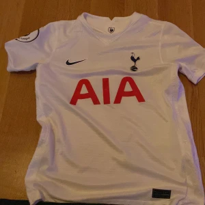 Tottenham Hotspur fotbollströja med Son 7 - Vit Tottenham Hotspur matchtröja från Nike med AIA sponsortryck, klubbmärke och Premier League-märke på ärmen. Nummer 7 och namnet Son på ryggen. Klassisk V-ringning och korta ärmar. Perfekt för Spurs-fans!  Från tottenhams hemsida bra kvalité 