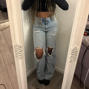 Ljusblå loose fit jeans med stora hål - Säljer ett par ljusblå loose fit jeans med hög midja och raka ben. Jeansen har stora slitningar och hål över knäna samt mindre slitningar framtill. Perfekta för en avslappnad och trendig look. Pris går att diskutera 