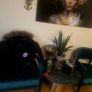 Svart dunjacka från Canada Goose med pälskant - Säljer en svart dunjacka från Canada Goose med huva och pälskant. Jackan har flera fickor framtill och klassisk logotyp på bröstet. Yttermaterialet är i polyester och bomull, fodrad med vitt ankdun och coyote-päls på huvan.