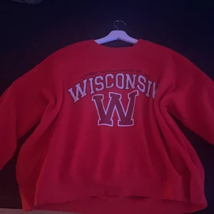 Röd sweatshirt  - Säljer en röd sweatshirt med stort Wisconsin-tryck på framsidan. Tröjan har en avslappnad passform och är perfekt för en casual look. Den är tillverkad i ett mjukt material som gör den bekväm att bära.