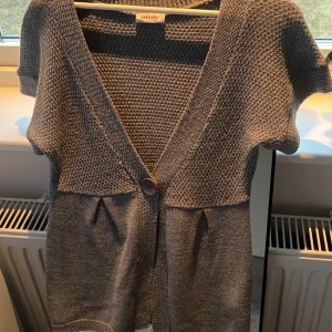 Grå kofta från Orsay - Säljer en stilren grå kofta från Orsay med korta ärmar och en stor knapp framtill. Koftan har en fin textur och är perfekt för lager-på-lager-stil. Passar bra till både jeans och kjol. Perfekt för kyliga dagar!