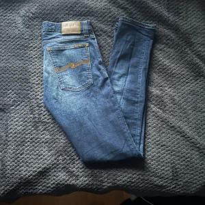 Blå jeans från Nudie Jeans - Snygga blå jeans från Nudie Jeans med klassisk femficksdesign och kontrastsömmar. De har en normal passform och är tillverkade i slitstarkt denim. Perfekta för en avslappnad stil. Riktigt bra skick🤩🤩 kontakta vid intressse/mer bilder!! 🚨Snabb affär=lägre pris🚨🚨