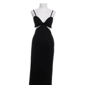 Svart långklänning från NA-KD - Elegant svart långklänning från NA-KD med smala axelband och en stilren design. Klänningen har en unik detalj med öppen rygg och knyt framtill som ger en modern touch. Perfekt för en kväll ute eller en speciell tillställning. Klänningen har en slits vid vänster sida 