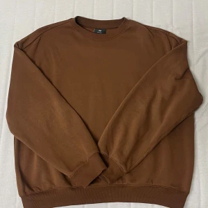Brun sweatshirt från H&M - Säljer en  brun sweatshirt från H&M i storlek M. Tröjan har en relaxed fit och är tillverkad av en bomullsblandning. Perfekt för en avslappnad stil med ribbade muddar vid ärmslut och nederkant. Använd endast en eller två gånger.