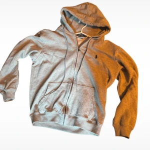 Grå hoodie från Ralph Lauren - En jäkligt snygg och skön zip hoodie från Ralph lauren. Den är i storlek m men skulle säga att den sitter som s då den är väldigt liten i storlek. Hör av er om ni har någon fråga!!