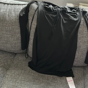 Svart klänning från Marthea - Snygg svart klänning från Marthea i storlek M. Tillverkad av 95% polyester och 5% elastan för en bekväm passform. Klänningen har långa ärmar och en stilren design med knytning framtill.