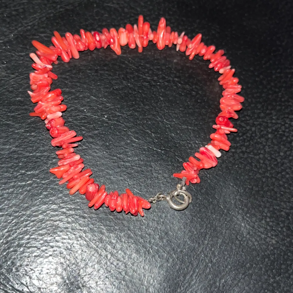 Snyggt armband med röda korallpärlor i olika former. Armbandet har ett enkelt lås i metall som ger en säker passform. Perfekt för att lägga till en färgklick till din outfit.. Asusteet.