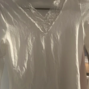 Vit långärmad topp från Gina Tricot - Säljer en stilren vit långärmad topp från Gina Tricot. Toppen har en vacker spetsdetalj vid den v-ringade halsen som ger en elegant touch. Perfekt för att lyfta vilken outfit som helst. Passar bra till både jeans och kjol.
