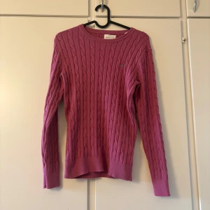 Rosa kabelstickad tröja från GANT - Säljer en snygg rosa kabelstickad tröja från GANT. Tröjan har långa ärmar och en rund halsringning. Perfekt för att hålla sig varm och stilren under kyligare dagar. 💖