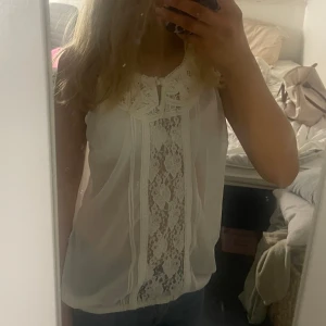 Vit spetsblus från Object - Säljer en vacker vit blus från Object med spetsdetaljer framtill och på ryggen. Blusen är ärmlös och har en luftig passform, perfekt för varmare dagar. Den har en elegant och romantisk stil som passar till många olika tillfällen. Säljer pågrund av att sen är lite stor på mig. 