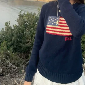 Mörkblå stickad tröja från Ralph Lauren - Säljer en snygg mörkblå stickad tröja från Ralph Lauren med en amerikansk flagga på bröstet. Tröjan har långa ärmar och ribbstickade muddar vid ärmslut och nederkant. Perfekt för en stilren look!
