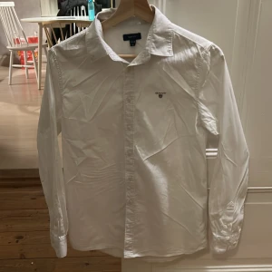 Vit skjorta från GANT - Säljer en klassisk vit skjorta från GANT i storlek 158/164 cm. Skjortan har långa ärmar och knappar framtill. Pris kan diskuteras 