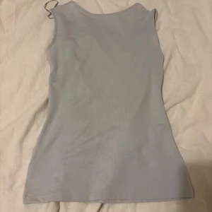 Ljusblå ärmlös linnetopp - Snygg ljusblå ärmlös linnetopp med djup rundad urringning. Perfekt för varma dagar eller som ett lager under en jacka. Enkel och stilren design som passar till det mesta.