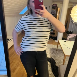 Vit och svart randig tröja stickad  - Säljer en stilren vit tröja med svarta ränder. Tröjan har korta ärmar och en normal passform, perfekt för en avslappnad look. Passar bra till jeans eller kjol.