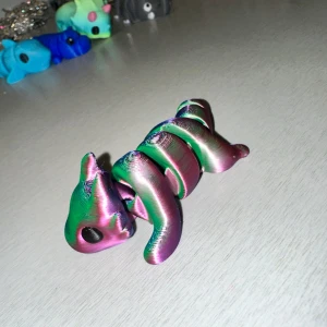 Flerfärgad spiralformad figur - En unik flerfärgad figur med en spiralformad kropp. Den har en metallisk yta som skiftar i grönt, rosa och lila. Figuren har en kattliknande form med stora ögon och en kompakt design.