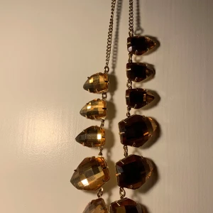 Guldigt halsband med stora stenar - Snyggt halsband med stora, facetterade stenar i guldton. Kedjan är tunn och elegant, vilket ger en fin kontrast till de större stenarna. Perfekt för att ge en glittrig touch till din outfit.