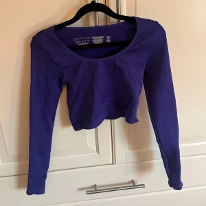 Lila långärmad croppad topp - Säljer en snygg lila långärmad topp från Gymshark. Den är croppad och har en rund halsringning. Perfekt för träning eller en avslappnad dag.