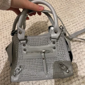 Grå axelväska med nitar - Snygg grå axelväska med nitar och dragkedja framtill. 
