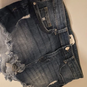 Blå jeansshorts med slitningar - Snygga blå lowwaist jeansshorts med slitna detaljer och fransiga kanter. Midjemåttet är 38 rakt över!!