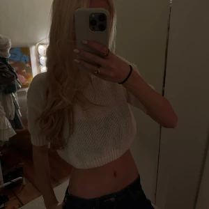 Vit stickad croppad tröja - Säljer en vit stickad croppad tröja med korta ärmar. Perfekt för en trendig och avslappnad stil. Passar bra till jeans eller kjol för en snygg look.