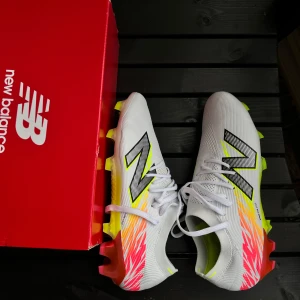 New Balance Furon V8 Elite FG - Snygga New Balance Furon V8 Elite FG fotbollsskor i vitt med färgglada detaljer i gult och rosa. Skorna har snörning och en lätt syntetisk ovandel för optimal prestanda på planen. Perfekta för spel på fasta gräsplaner.