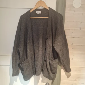 Grå kofta från Monki - Säljer en mysig grå kofta från Monki i storlek S. Koftan har en loose passform med knappar framtill och fickor. Perfekt för kyligare dagar. 🧥