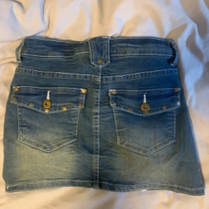 Jeanskjol med knappar - Snygg jeanskjol i klassisk blå denim med knappar och fickor både fram och bak. Kjolen har en kort längd och en stilren design med dekorativa sömmar. Perfekt för en lite ”vintage” look. Den är även något stretchig och formar sig bra efter kroppen💕pris diskuterbart vid snabb affär