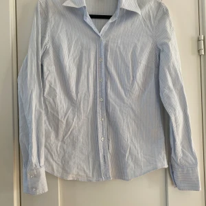 Blåvit randig skjorta från GANT - Säljer en stilren blåvit randig skjorta från GANT. Skjortan har långa ärmar och knappar framtill. Perfekt för en klassisk look. Blå och vit randig skjorta i strl 38 från Gant.  Använd men i fint begagnat skick förutom att skjortan är lite lätt missfärgad på kragen i nacken.  Mått Över bröstet: ca 48 cm Längd från axeln och ner: ca 64 cm  97% bomull och 3% elastan  Kommer från ett djur och rökfritt hem.