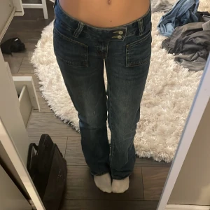 Blå jeansbyxor från 157 - Snygga blå jeansbyxor från 157 i storlek XS. Byxorna har en lågmidjad design med knappar framtill och raka ben. Perfekta för en avslappnad stil. 