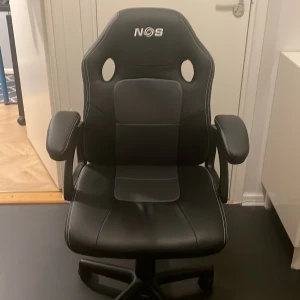 Gamingstol NOS  - En bra junior gamingstol. Är lite sönder på baksidan men syns inte jätte mycket men syns att det är använd. Går att höja och sänka med en spak på sidan.