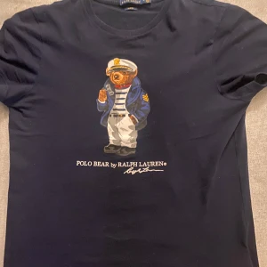 Svart t-shirt med Polo Bear från Ralph Lauren - Snygg marinblå t-shirt från Ralph Lauren med det ikoniska Polo Bear-trycket på framsidan.      Utmärkt skick, nypris cirka 1200kr