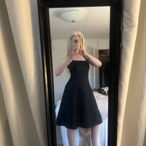 Svart halterneck klänning från Sixth Sense - Elegant svart klänning från Sixth Sense med halterneck och subtilt blommönster. Perfekt för en stilren look med en vacker passform som framhäver figuren. Klänningen har en klassisk design som passar många tillfällen.