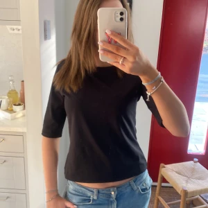 Svart kortärmad topp - Säljer en  svart topp med korta ärmar. Perfekt för en avslappnad look. Toppen har en enkel design och är lätt att matcha med olika outfits. Den går ut i midjan. 
