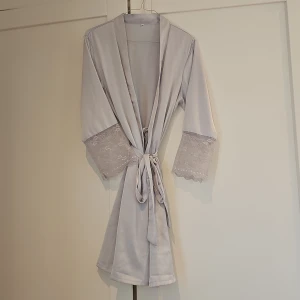 Ljusgrå morgonrock med spetsdetaljer - Elegant ljusgrå morgonrock med vackra spetsdetaljer på ärmarna. Den har ett knytband i midjan för en justerbar passform. Perfekt för en lyxig och bekväm känsla hemma. Står storlek XXL på men passar perfekt alla storlekar då den har knytband och är rätt liten i storlek. 