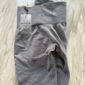 Grå leggings från NVGTN - Snygga grå leggings från NVGTN med hög midja och elastiskt material. Perfekta för träning eller en avslappnad dag. De har en stilren design med diskret logga på midjebandet. Storlek S. Endast testade 