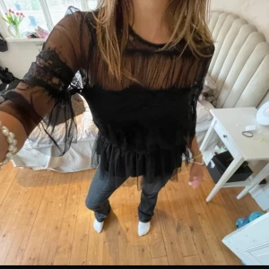 Svart spetsblus från happy Holly - Snygg svart blus från happy holly med transparent spets och volangdetaljer. Blusen har långa ärmar och en elegant design som passar perfekt för en stilfull look. Perfekt för att lyfta vilken outfit som helst!