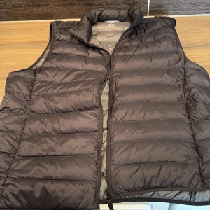 Svart dunväst  - Säljer en stilren svart dunväst från Uniqlo. Västen har en dragkedja framtill och är perfekt för kyligare dagar. Den är lätt och smidig att bära med sig. Passar bra för både vardag och utomhusaktiviteter. 