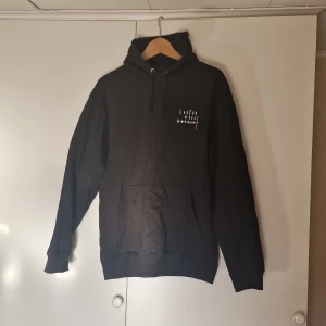 Svart hoodie med Laxton logga fram bak - Säljer en svart hoodie med tryck både fram och bak av Laxton. Den har en stor ficka framtill och justerbar huva med dragsko. Perfekt för en avslappnad stil. Aldrig använt
