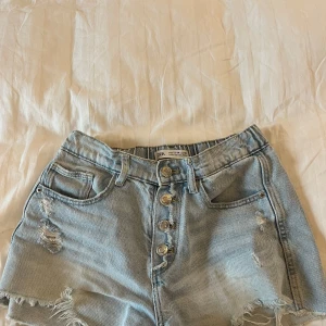 Ljusa jeansshorts från Zara - Snygga ljusa jeansshorts från Zara med slitna detaljer och knappar framtill. Perfekta för en avslappnad stil. Shortsen har en klassisk femficksdesign och är tillverkade i ett bekvämt denimtyg.