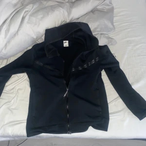 Svart hoodie från Nike - Svart Nike tech fleece, passar bra som en uppvärmnings tröja men jag har själv aldrig använt den till det men haft den när jag varit med kompisar eller som under ställ när jag varit ute annars är den helt ren inga fläckar eller defekter. Pris kan diskuteras  vid smidig affär