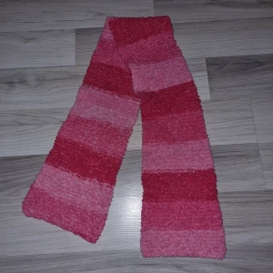 Rosa-randig halsduk - Säljer en supermjuk och fluffig halsduk i olika nyanser av rosa. Den har breda ränder och är perfekt för att hålla dig varm under kyliga dagar. Halsduken är ungefär 100 cm lång och ger en mysig känsla.
