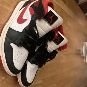 Nike Air Jordans i svart, vitt och rött - Snygga Nike Air Jordans i klassisk färgkombination av svart, vitt och rött. Skorna har en hög design med snörning och den ikoniska Air Jordan-loggan på sidan. Perfekta för sneakerheads som vill ha en tidlös stil.