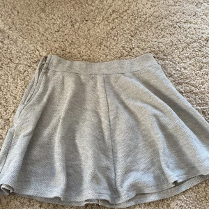 Grå kjol från Zara Girls - Säljer en ljusgrå kjol från Zara Girls med lätt utställd passform. Kjolen har en bred linning och stängs med dragkedja i sidan. Perfekt för en enkel och stilren look.