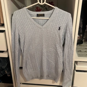 Ljusblå kabelstickad tröja från Polo Ralph Lauren - Säljer en ljusblå kabelstickad tröja från Polo Ralph Lauren med v-ringning och broderad logga på bröstet. Tröjan har lång ärm och ribbade muddar vid ärmslut och nederkant. Storlek L men känns som storlek s-m. 