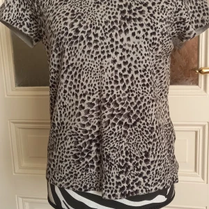 Gråsvart leopardmönstrad t-shirt från Charter Club - Snygg t-shirt från Charter Club i grått och svart med leopardmönster. Modellen har korta ärmar och rund halsringning. Perfekt för dig som vill sticka ut med ett djurmönster i din vardagsstil.