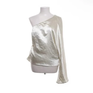 Champagnefärgad oneshoulder-top från Gina Tricot - Säljer en glansig, champagnefärgad oneshoulder-top från Gina Tricot. Toppen har lång ärm på ena sidan och är axelbandslös på andra sidan. Tillverkad i ett satinliknande material som ger en lyxig känsla.