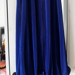 Blå plisserad långklänning med knytband - Säljer en blå långklänning med plisserat tyg och knytband vid halsen. 